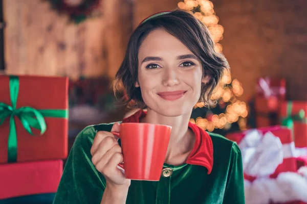 Fénykép a pozitív vidám hölgy tart csésze ital kakaó élvezze x-mas este viselni elf jelmez díszített iroda beltérben — Stock Fotó