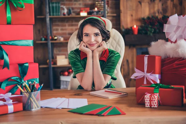 Fotografie mladé veselý šťastný pozitivní Santa pomocník žena sedět stůl ruce tvář úsměv uvnitř domu doma — Stock fotografie