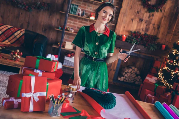 Φωτογραφία από χαριτωμένο λαμπερό νεαρή κοπέλα φορούν ρούχα ξωτικό κρατώντας ψαλίδι συσκευασία το νέο έτος παρόν χαμογελώντας σε εσωτερικούς χώρους σπίτι δωμάτιο — Φωτογραφία Αρχείου