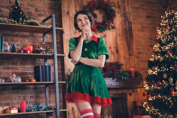 Photo de charmante jeune femme rêveuse habillée costume vert souriant célébrant la nouvelle année bras menton intérieur chambre maison — Photo