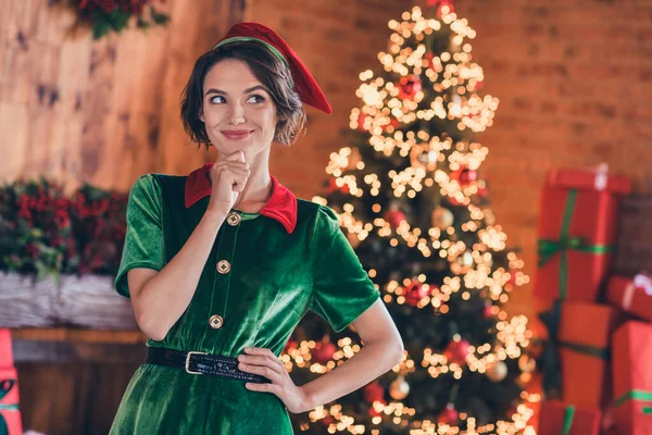 Φωτογραφία από λαμπερό στοχαστική νεαρή γυναίκα ντυμένος πράσινο κοστούμι χαμογελώντας γιορτάζει το χέρι το νέο έτος πηγούνι εσωτερικό δωμάτιο σπίτι — Φωτογραφία Αρχείου