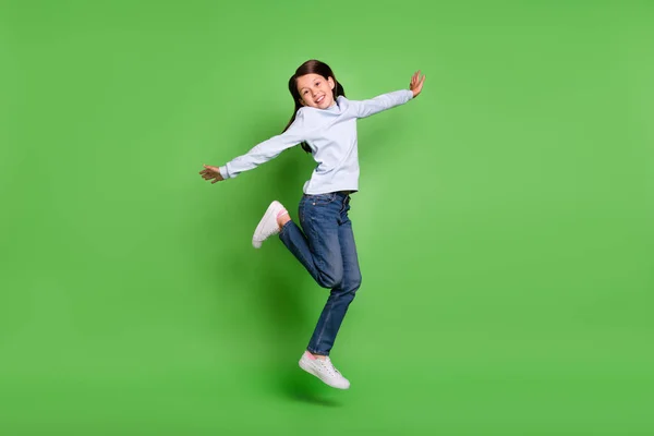 Фото милої красивої школярки, що носить синій черепаха, стрибає з високими сторонами рук, усміхаючись ізольований зелений колір фону — стокове фото