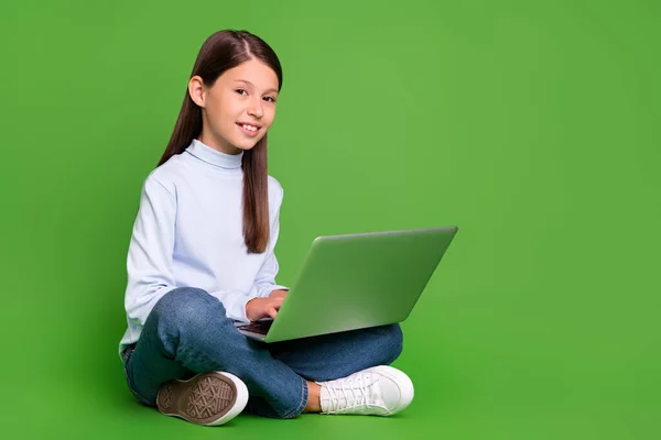 Foto van leuke mooie school meisje gekleed blauwe coltrui zittende vloer chatten moderne gadget lege ruimte geïsoleerde groene kleur achtergrond — Stockfoto