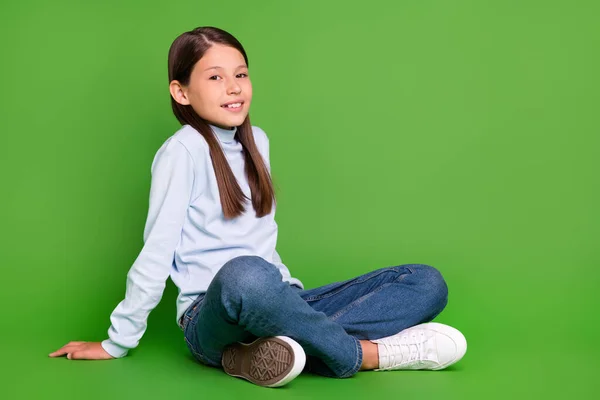 Φωτογραφία από γοητευτικό χαριτωμένο κορίτσι σχολείο ντυμένος μπλε ζιβάγκο καθιστικό κενό χώρο χαμογελώντας απομονωμένο πράσινο χρώμα φόντο — Φωτογραφία Αρχείου