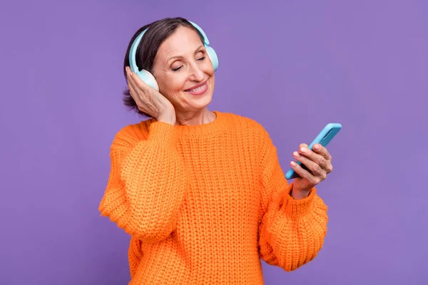 Foto de anciana jubilada escuchar lista de reproducción auriculares cambiar canción teléfono celular aislado sobre fondo de color púrpura —  Fotos de Stock