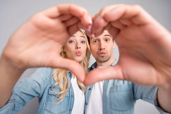 Foto de jovem casal despojado lábios enviar ar beijo mostrar dedos coração símbolo amor dia dos namorados isolado sobre fundo de cor cinza — Fotografia de Stock