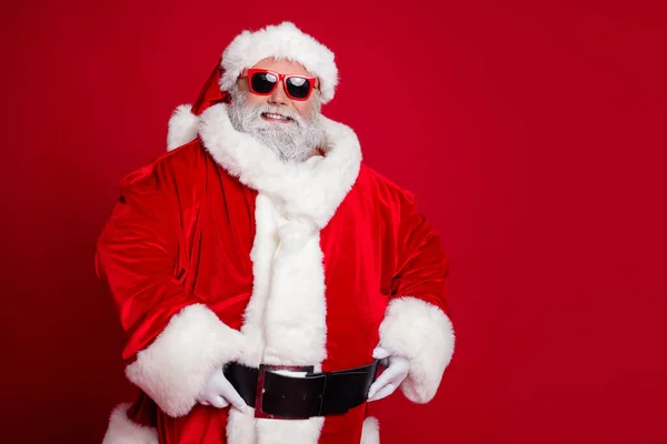 Foto van vrolijke positieve zelfverzekerde gepensioneerde man handen riem dragen kerstman hoed kostuum geïsoleerde rode kleur achtergrond — Stockfoto