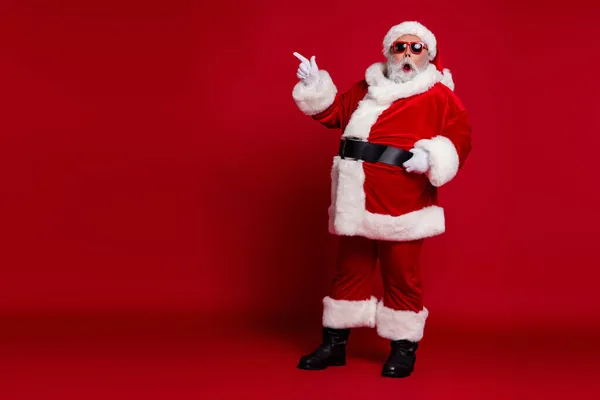 Zdjęcie podekscytowany szalony człowiek wskazują palec pusty przestrzeń nowość nosić Santa kapelusz kostium odizolowany czerwony kolor tła — Zdjęcie stockowe
