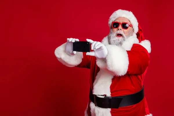 Portret van aantrekkelijke bebaarde verbaasd grappige Kerstman met behulp van apparaat maken selfie vlog geïsoleerd over felrode kleur achtergrond — Stockfoto