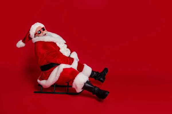 Foto van funky gekke oude man rijden slee hebben x-mas plezier dragen kerstman hoed kostuum geïsoleerde rode kleur achtergrond — Stockfoto