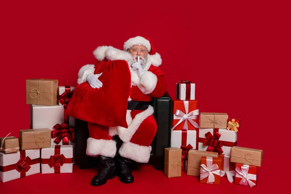 Full size foto van onder de indruk santa hold bag met cadeautjes dragen cap brillen jas broek schoenen geïsoleerd op rode achtergrond — Stockfoto