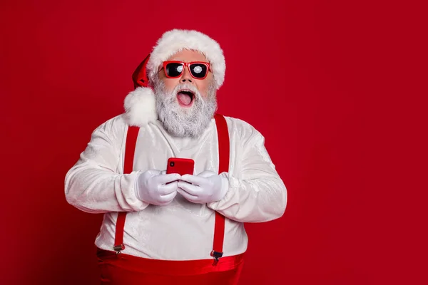 Фото сумасшедшего старика держать телефон положительные отзывы реакции носить подтяжки Санта шляпа изолированный красный цвет фона — стоковое фото