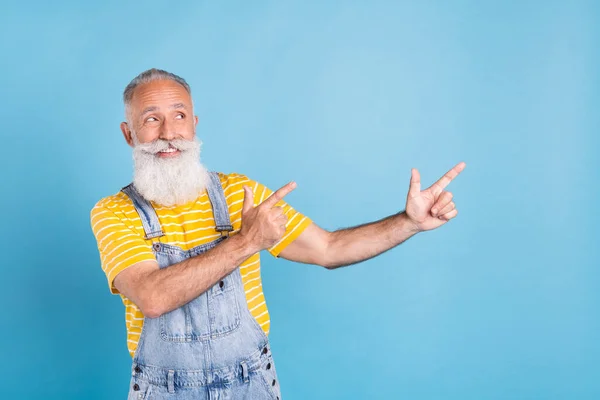 Фото смішного старого білого чоловіка, який вказує на порожній простір, носить жовту футболку загалом ізольовано на синьому кольорі — стокове фото