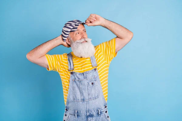 Foto di bello invecchiato grigio uomo sguardo vuoto spazio usura cappello giallo t-shirt complessivamente isolato su sfondo di colore blu — Foto Stock