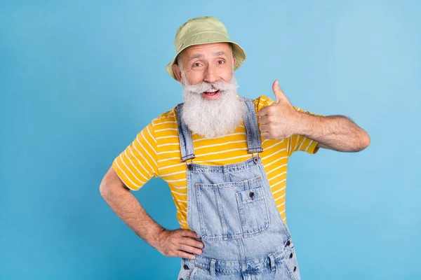 Photo de vieil homme gris impressionné montrer pouce vers le haut porter chapeau t-shirt jaune dans l'ensemble isolé sur fond de couleur bleue — Photo