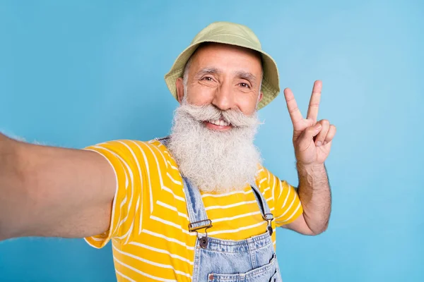 Photo de l'homme âgé heureux sourire positif faire selfie montrer paix cool v-signe isolé sur fond de couleur bleue — Photo