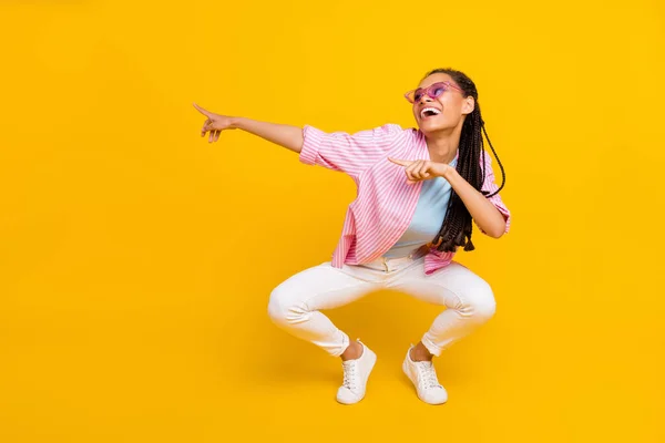 Photo of excited african lady direct fingers empty space wear sunglass striped shirt isolated yellow color background — Stock Photo, Image