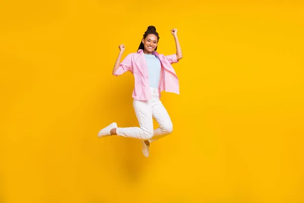 明るい女性のジャンプの写真は、達成幸運を喜びますストライプのシャツを着用孤立黄色の背景 — ストック写真