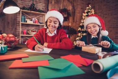 Portrait of two attractive cheerful siblings preparing eve time writing letters wish dream packing gifts at brick loft home indoors clipart