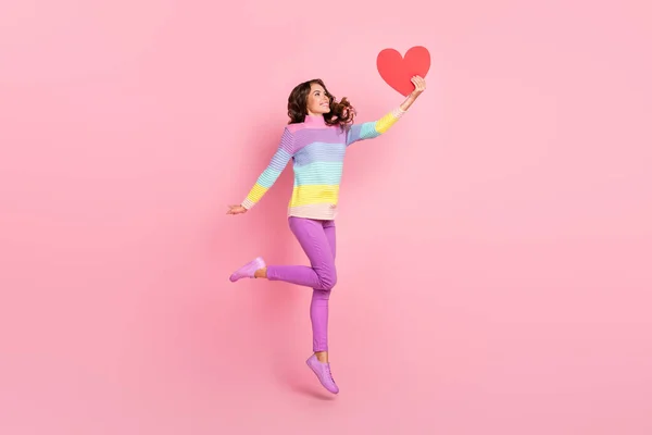 Полноразмерная фотография юной мечтательной девушки, прыгающей вверх по бумажному сердцу подруги, изолированной на цветном фоне — стоковое фото