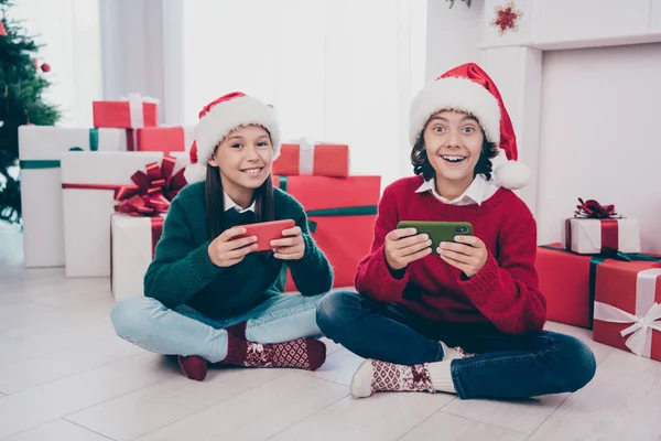 Zdjęcie dwójki funky dzieci posiadają telefon cieszyć X-mas odzieży wypoczynkowej jumper kapelusz w urządzone domu w pomieszczeniach — Zdjęcie stockowe