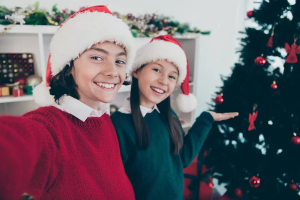 Photo of two bonding children make selfie girl invite comfy apartment wear jumper hat in decorated home indoors — Stock Photo, Image