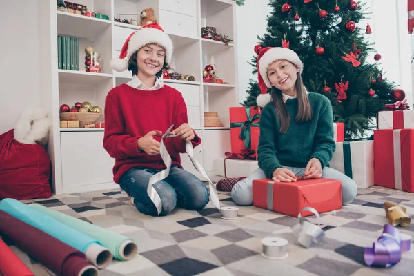 Фото веселых детей помощники сидят пол подготовить декабрьские подарки носить шляпу x-mas свитер в украшенном доме в помещении — стоковое фото