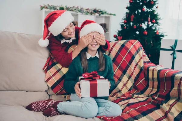 Foto de bonito niño cerrar los ojos hermana preparar sorpresa regalo desgaste x-mas sombrero jersey en casa decorada en interiores —  Fotos de Stock