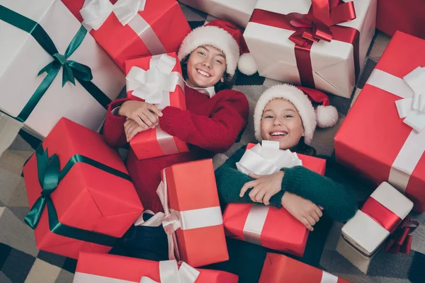 Zdjęcie uroczych małych dzieci leżały podłogi objąć obecny pudełko nosić x-mas kapelusz sweter w urządzone domu w pomieszczeniach — Zdjęcie stockowe
