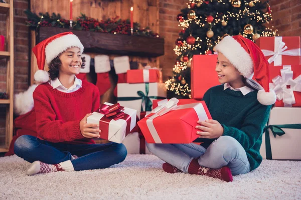 Портрет двух привлекательных веселых братьев и сестер, сидящих на ковре, разделяя подарки накануне праздничного отдыха на чердаке дома — стоковое фото