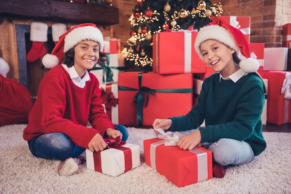 Porträt von zwei attraktiven, fröhlichen Geschwistern, die auf dem Teppich sitzen und Geschenkboxen öffnen — Stockfoto
