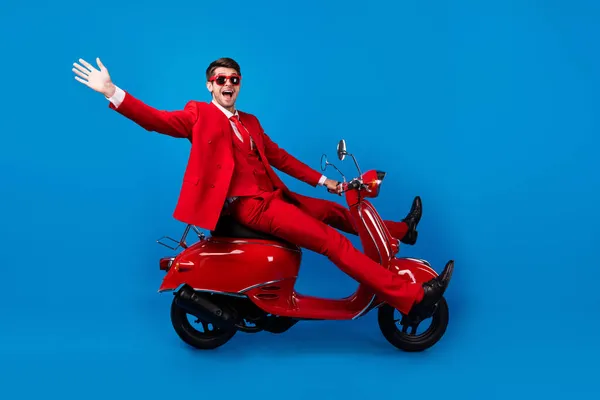 Full body profile side photo of young guy happy positive smile waving hand hello drive scooter isolated over blue color background — Stock Photo, Image