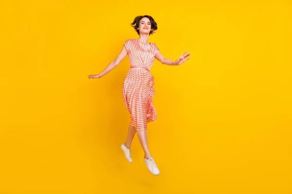 Foto de sonho menina salto desfrutar de voo passo desgaste listrado vestido tênis isolado cor amarela fundo — Fotografia de Stock
