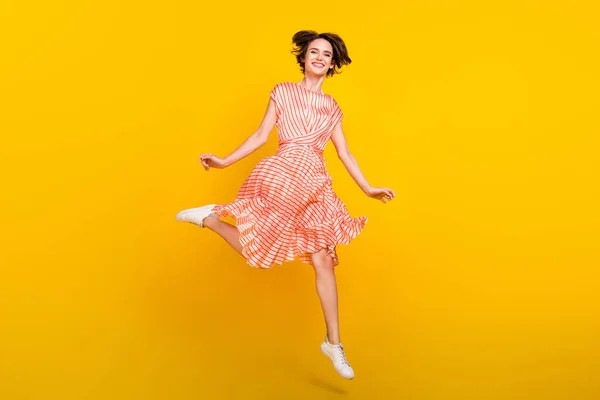 Foto de louco despreocupado menina salto desfrutar de fim de semana desgaste listrado vestido tênis isolado cor amarela fundo — Fotografia de Stock
