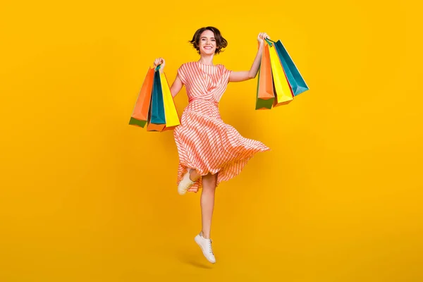 Photo of shopaholic active girl jump hold bargains wear striped dress sneakers isolated yellow color background — Stock Photo, Image