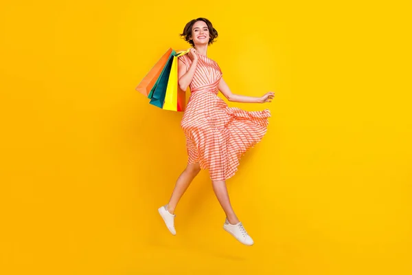 Foto de linda menina bonita salto transportar pacotes de shopping desgaste vestido listrado calçado isolado cor amarela fundo — Fotografia de Stock