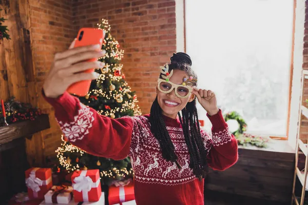 Φωτογραφία της θετικής κυρία κρατήσει τηλέφωνο λάβει selfie ακτινοβολούν χαμόγελο φορούν ελάφια πουλόβερ γυαλιά σε διακοσμημένο σπίτι σε εσωτερικούς χώρους — Φωτογραφία Αρχείου