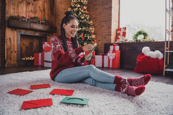Foto av positiv dam sitta matta hålla telefon läsa x-mas sociala medier bära pullover i dekorerade hem inomhus — Stockfoto