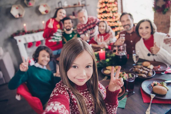 Фото портрет маленькая девочка в свитере празднует зимние праздники с семьёй делает селфи показывая V-знак — стоковое фото