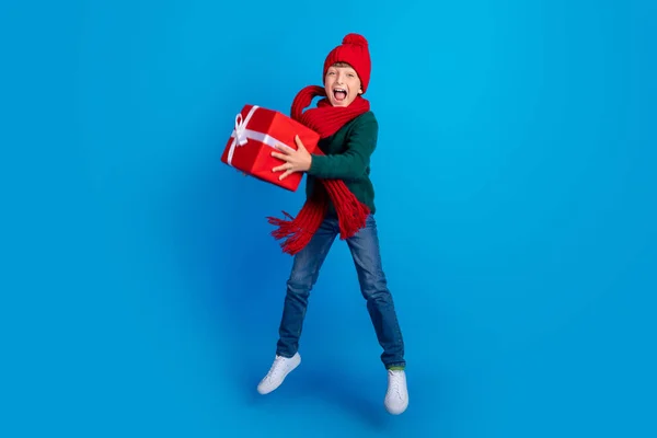 Фотография мальчика в полный рост, прыгающего, держа xmas на изолированном ярко-синем фоне — стоковое фото