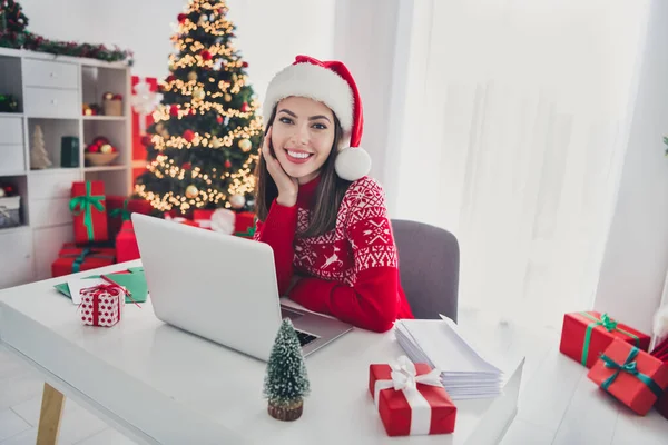 Foto von Fernarbeiterin Dame sitzen Arbeitsplatz Netbook tragen Weihnachtsmann Hut Pullover in dekoriert Weihnachten zu Hause drinnen — Stockfoto