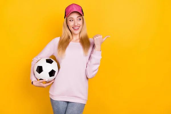 Foto von jungen attraktiven Mädchen glücklich positives Lächeln halten Fußball Daumen leeren Raum Anzeige isoliert über gelben Farbhintergrund — Stockfoto