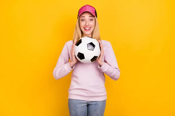 Foto ritratto donna sorridente in cap mantenendo palla da calcio ridere felice isolato luminoso colore giallo sfondo — Foto Stock