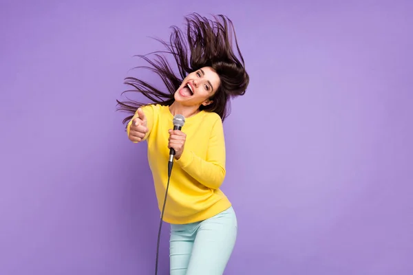 Zdjęcie wesoły młody pozytywny kobieta punkt palec latać włosy mikrofon piosenkarka karaoke izolowane na fioletowy kolor tła — Zdjęcie stockowe