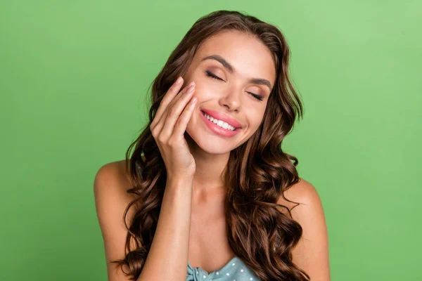 Фото молодой девушки счастливой позитивной улыбкой руки касаются щеки чистый мягкий увлажнение кожи изолированы на зеленом фоне цвета — стоковое фото