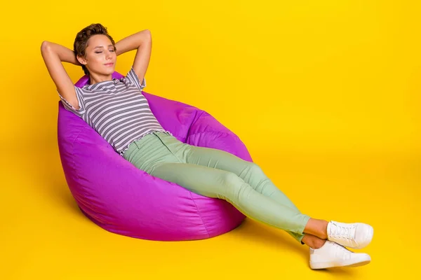 Foto em tamanho completo de menina sonolenta sentar no saco desgaste t-shirt jeans sapatilhas isoladas no fundo amarelo — Fotografia de Stock