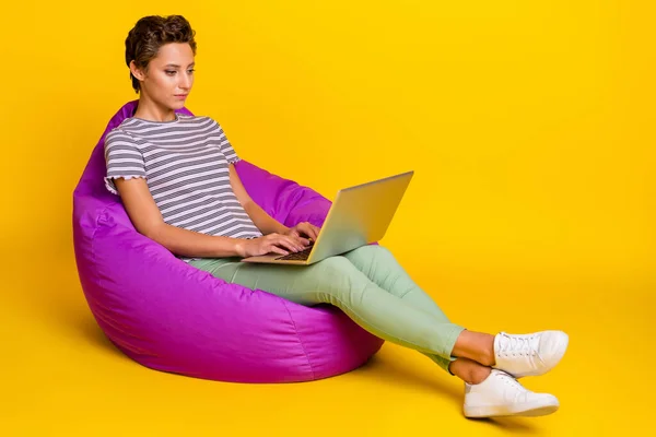 업무용 노트북에 앉아 있는 사장 밀레니엄 아가씨의 전신 프로필 사진노란 배경에 분리 된 티셔츠 청바지 스니커즈를 입고 있는 모습 — 스톡 사진