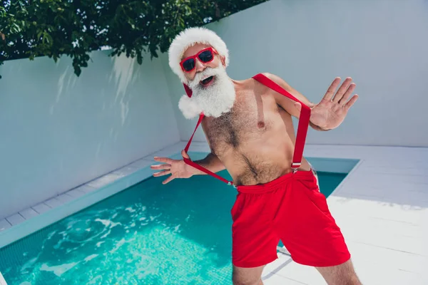 Ritratto di attraente allegro ragazzo Babbo Natale dai capelli grigi ingannare tirando bretelle divertirsi trascorrere vigilia dell'avvento all'aperto — Foto Stock