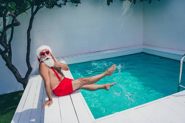 Foto van behoorlijk geschokt santa claus dragen rode shorts arm wang jukbeen koud water vieren noel buiten villa spa-hotel — Stockfoto