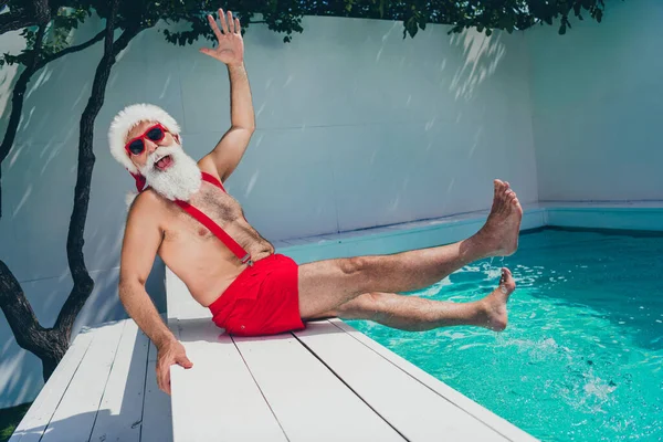Foto di divertente funky Babbo Natale indossare pantaloncini rossi sorridente godendo dell'acqua della piscina che celebra il Natale all'aperto villa spa-hotel — Foto Stock